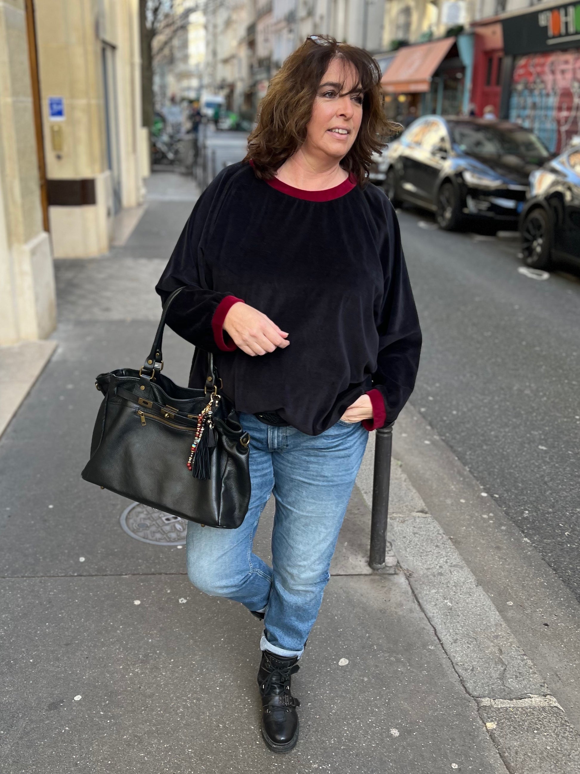 sweat grande taille en velours pour femme. Noir avec cool et poignets rouges. De face, femme marchant dans la rue