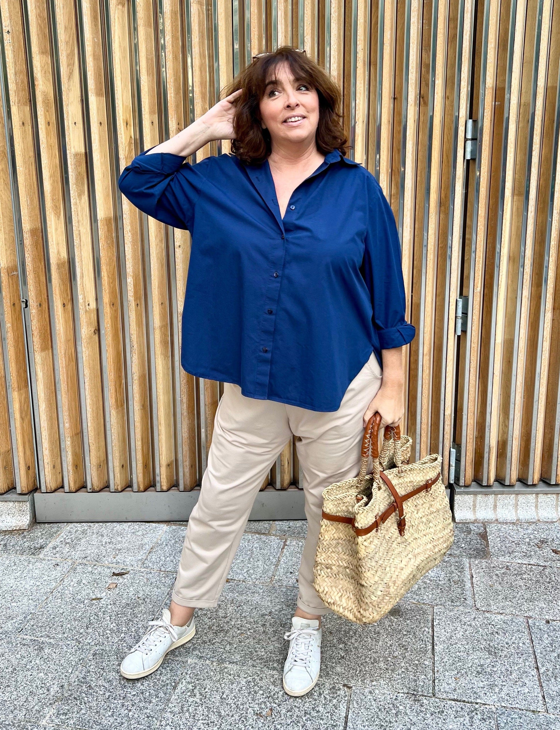 chemise grande taille femme bleu marine, portée avec pantalon beige de face et un panier en osier et en cuir